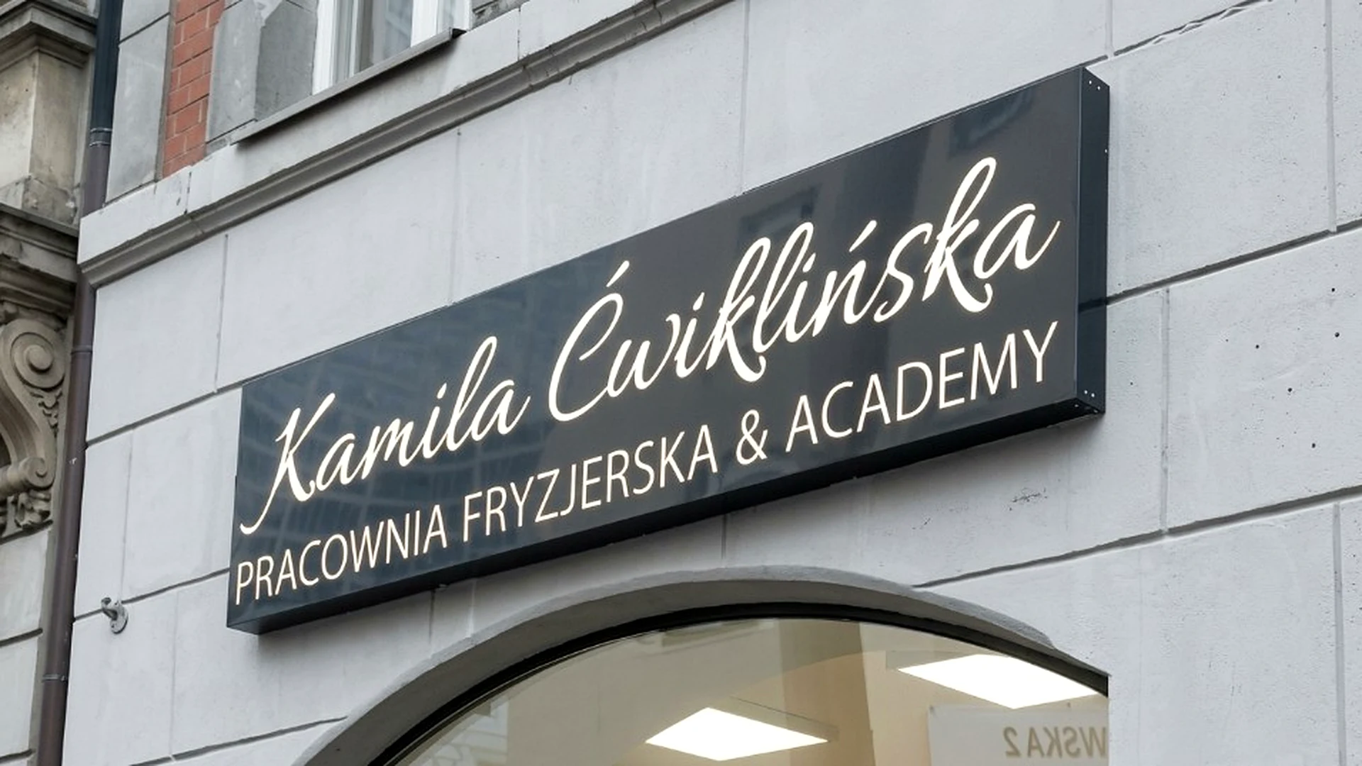 Czarny szyld pracowni fryzjerskiej Kamila Ćwiklińska
